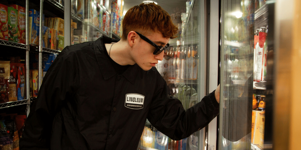 man in street wear opening a fridge from a local convenience store